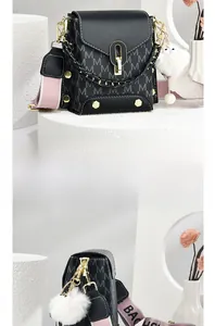 Detail of black faux leather handbag with M-letter pattern, gold lock and plush charm
