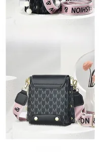 Detail of black leather crossbody bag with gray M-pattern and pink wide woven shoulder strap