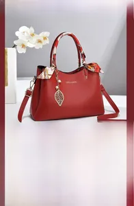 Detail of red lychee leather handbag with silk scarf handle and gold leaf pendant
