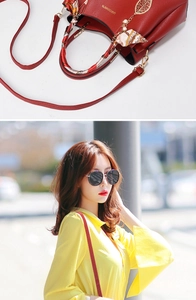 Detail of red pebbled leather handbag with gold logo, decorative silk scarf and leaf charm
