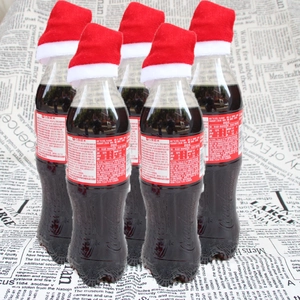 Mini bonnets de Noël rouges décorant des bouchons de soda sur fond de vieux journal