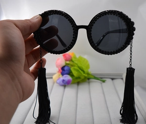 Detail of round oversized sunglasses with handmade black rhinestones and long tassel chains