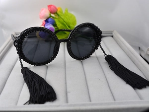 Detail of round sunglasses featuring black bead embellishments and hanging silk tassels