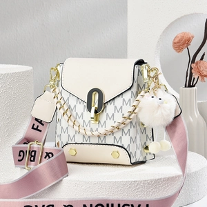 Chic cream monogram crossbody bag with pink strap and plush charm on geometry stand