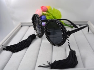Detail of round oversized black sunglasses featuring rhinestone borders and long silk tassels