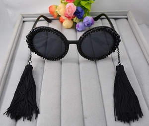 Macro detail of round black sunglasses featuring bead trim and hanging chain tassels