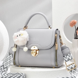 Detail van grijze leren handtas met gouden draaisluiting en geweven crossbody riem