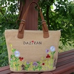 Close-up of woven straw tote bag featuring hand-painted floral patterns and leather handles