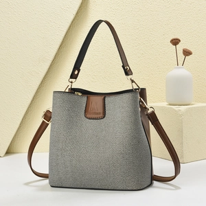 Detail of the bucket bag's gray woven texture and brown leather adjustable shoulder strap