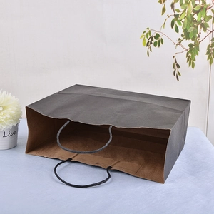Detail of dark grey kraft paper gift bag with black twisted rope handles on a desk