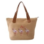 Detail of flamingo embroidery on a straw tote bag with brown leather handles