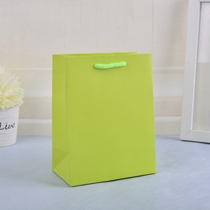Detail of yellow-green paper shopping bag with twisted rope handles on blue surface