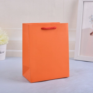 Close-up of orange paper shopping bag with red rope handles in a modern home setting