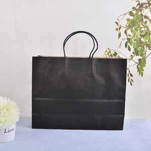 Detail shot of a plain black paper gift bag with twisted handles on a blue surface