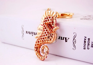 Detailed close-up of a golden seahorse keychain with pink rhinestones on a book