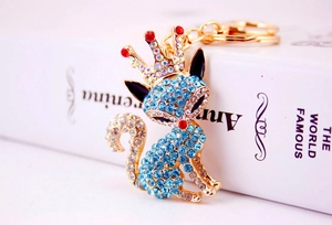 Détail d'un porte-clés renard en strass bleus avec couronne dorée à côté d'un livre