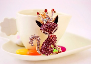 Detail view of pink rhinestone fox keychain with gold crown on white ceramic cup