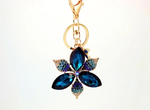 Detail of a golden metal keychain featuring a flower pendant with deep blue crystals