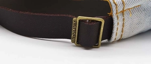Detail of adjustable leather strap and bronze metal buckle on denim baseball cap