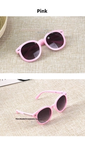 Pink round frame kids sunglasses with metal arrow accents on a woven beige mat