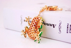 Close-up of golden frog keychain with green enamel details and hollow metal design