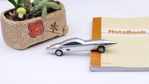 Silver car-shaped creative pen resting on a notebook with a potted succulent plant