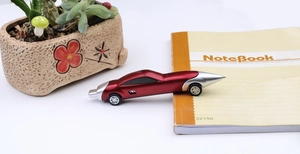 Creative red racing car shaped ballpoint pen with wheels on a white desk workspace