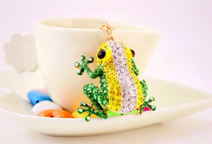 Close-up of cute green crystal frog pendant with rhinestones on a white cup edge
