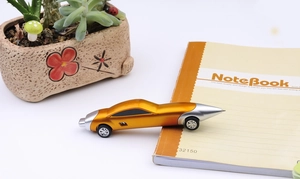 Close-up of orange car-shaped ballpoint pen placed on a notebook with white background