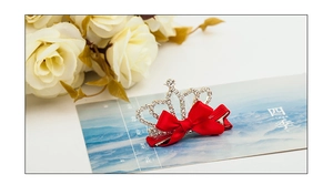 Detail of crystal crown hair clip with red satin bow on floral decorative card