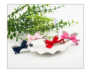 Close-up of four colorful bow hair clips with rhinestones on a white ceramic plate