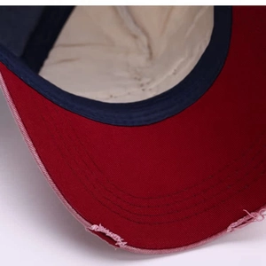 Detail of distressed red brim with frayed edges and contrast stitching on a baseball cap