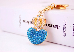 Close-up of golden crown heart keychain with blue rhinestones next to a book
