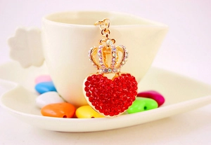 Detailed close-up of a gold crown and red heart keychain on a decorative white cup