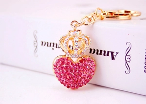 Close-up of pink rhinestone heart keychain with gold crown on book surface