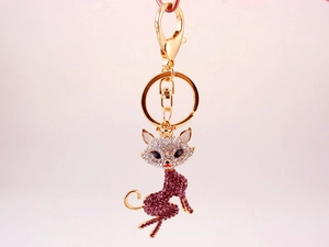 Macro detail of cat keychain with purple crystals and gold metal on pink background