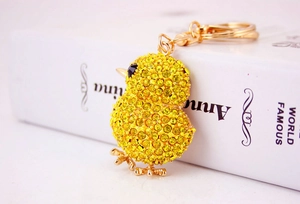 Close-up of a gold-toned cartoon chicken keychain with yellow rhinestones on a book