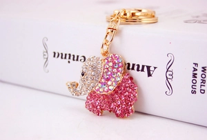 Close-up of golden elephant keychain with sparkling pink crystals on white book background