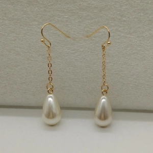 Detail view of teardrop pearl earrings with golden chains on a textured background