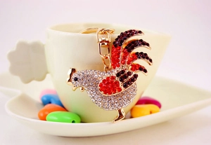 Dettaglio del portachiavi a forma di gallo dorato con strass su una tazza di ceramica