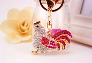 Detail of a sparkling rooster keychain featuring white and pink rhinestones on gold metal