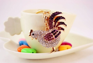 Macro di un portachiavi a forma di gallo con strass viola e bianchi in una tazza
