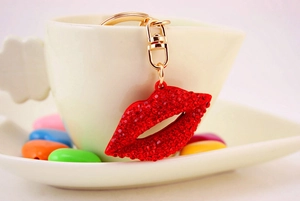 Macro detail of red rhinestone lips keychain with gold lobster clasp on white ceramics