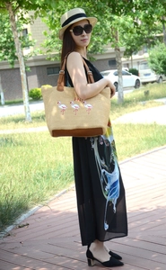 Detail of a straw tote bag with pink flamingo embroidery and brown leather straps