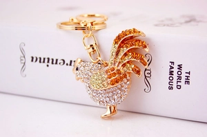 Detailed close-up of a golden rooster keychain encrusted with white and orange rhinestones