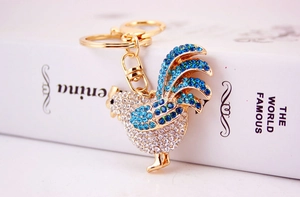 Close-up of golden rooster keychain with sparkling white and blue rhinestones and lobster clasp