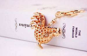 Detailed view of a golden rooster keychain with intricate hollow floral patterns on a book