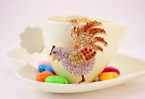 Dettaglio di un portachiavi a forma di gallo con strass colorati appeso a una tazza