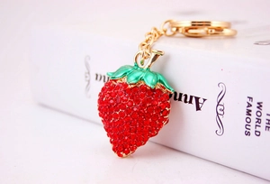 Close-up of strawberry keychain with red rhinestones and green leaves on white book