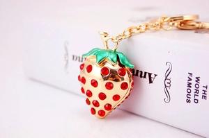 Close-up of golden strawberry keychain with red crystals and green enamel leaves
